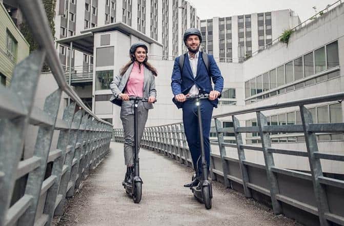 A man and a woman dressed in formal attire crossing a bridge onboard their Segway Ninebot Kickscooter Max